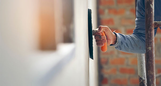 Person using a trowel to apply plaster on a wall, showcasing home improvement or construction work.