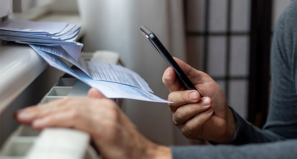 A person holding a smartphone in one hand while examining papers on a radiator, highlighting the importance of efficient paperwork management.