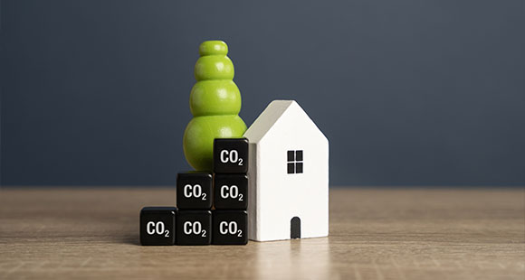 A small white house next to a green tree and black blocks labeled CO2, symbolizing environmental concepts and sustainability.